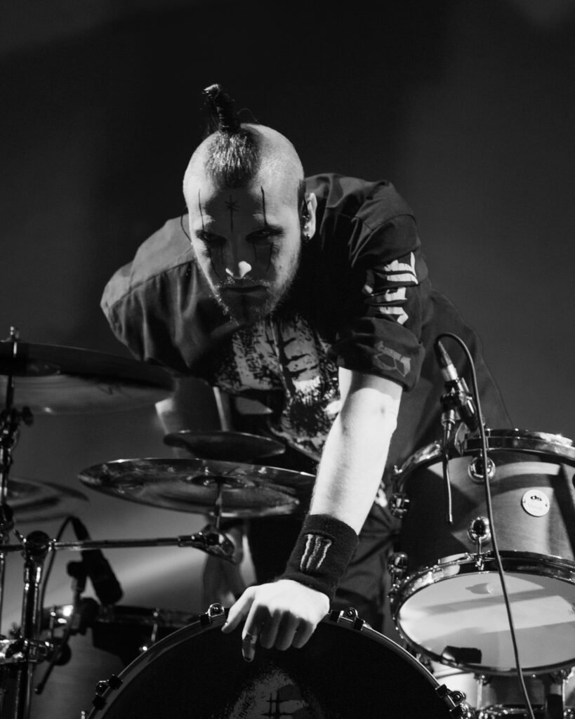 Black-and-white photograph of a long-haired drummer leaning over the drum kit