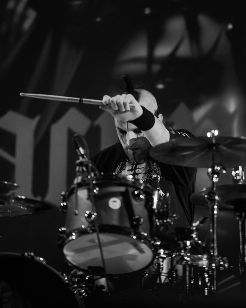 Black-and-white photograph of a drummer holding a microphone at the drum kit
