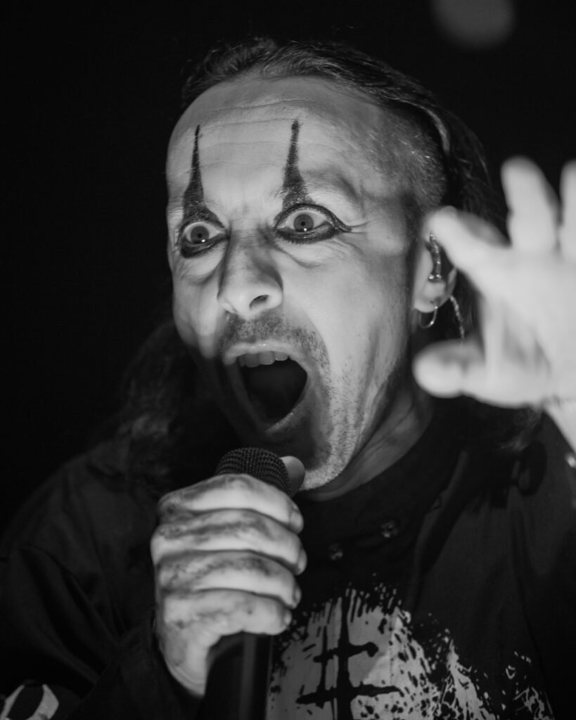 Black-and-white close-up of a singer with face paint holding a microphone