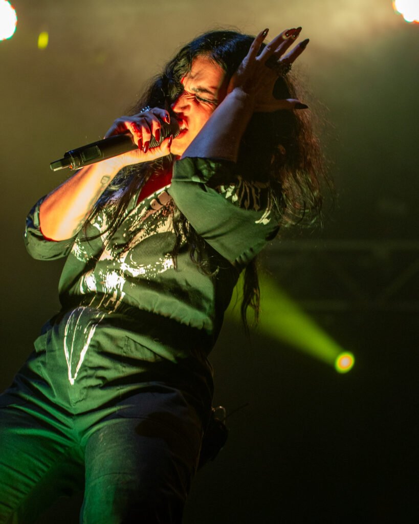 Vocalist singing and reaching towards the audience under green lighting
