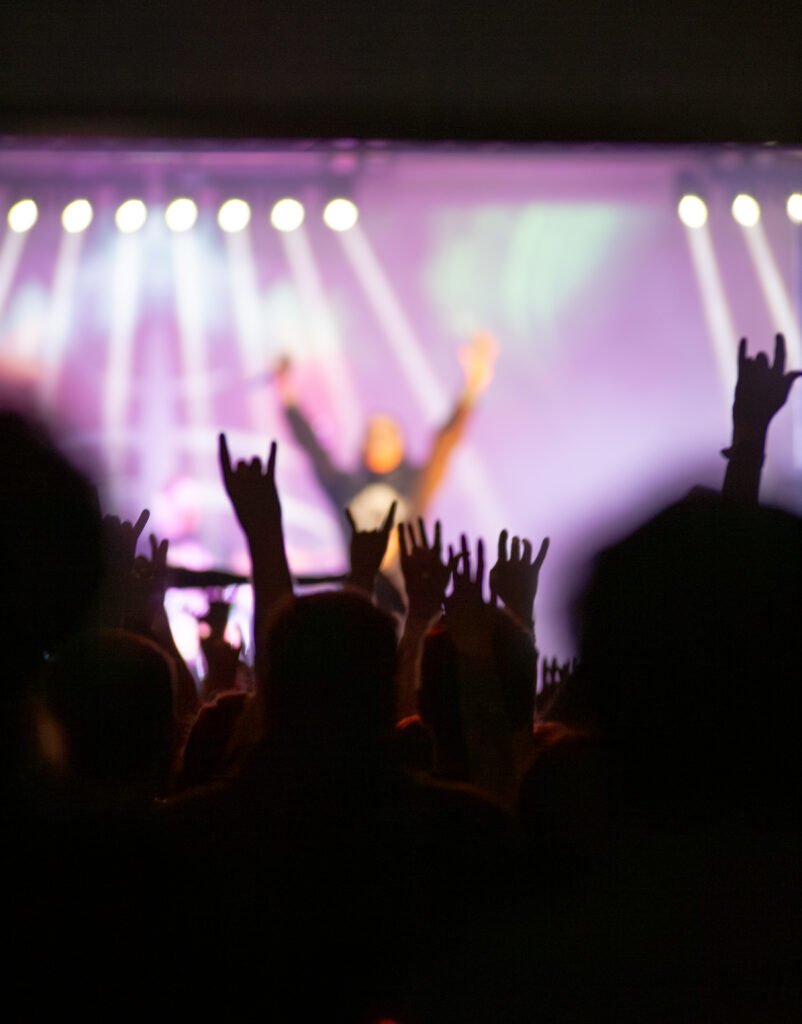 Raised hands in a crowd beneath purple concert lighting
