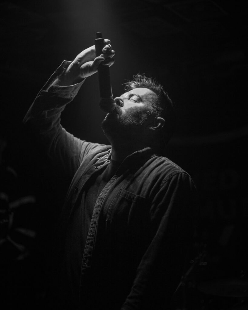 Black-and-white low-angle photograph of a performer holding a microphone