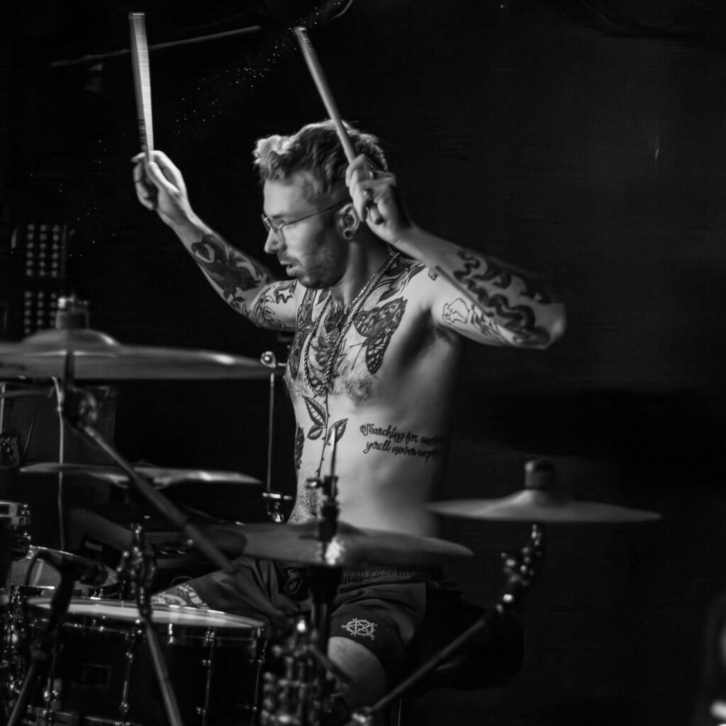 Black-and-white photograph of a drummer with both sticks raised