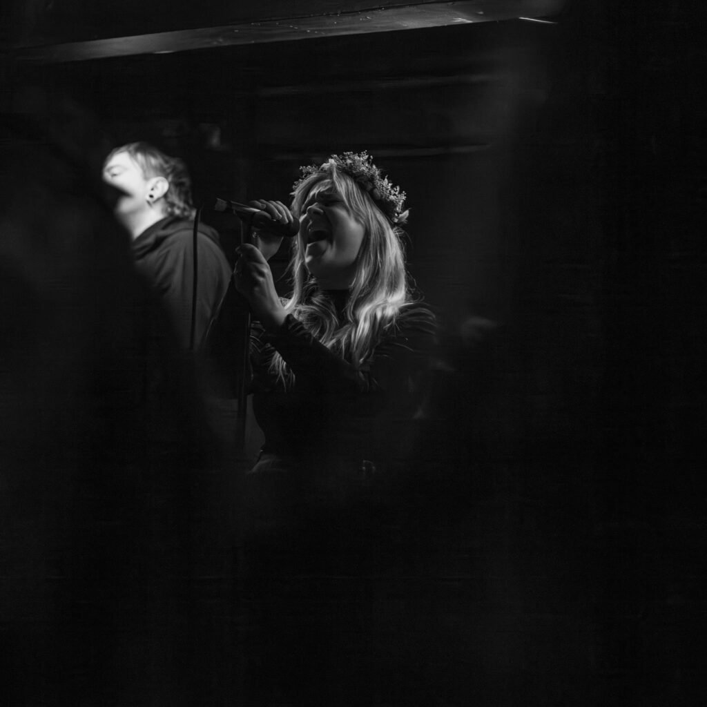 Black-and-white photograph of a long-haired musician performing on a dark stage