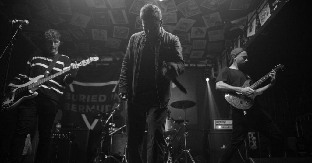 Black-and-white photograph of a vocalist, bassist and guitarist performing on stage