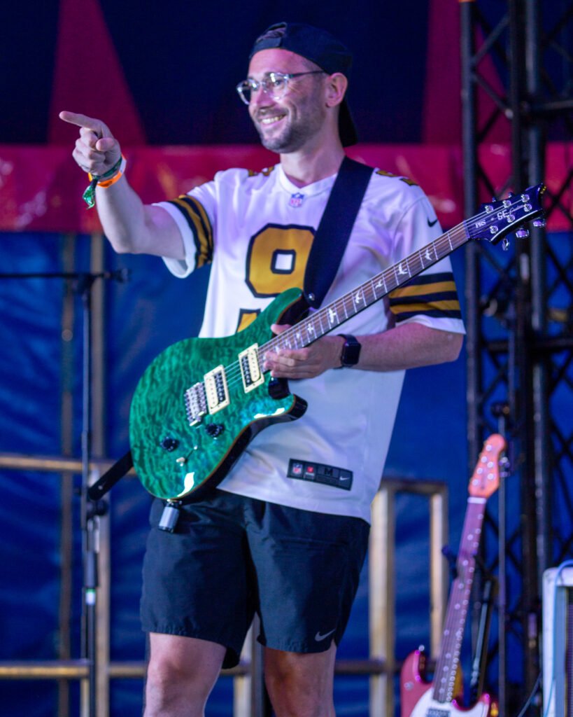 Guitarist playing a green electric guitar under coloured stage lighting