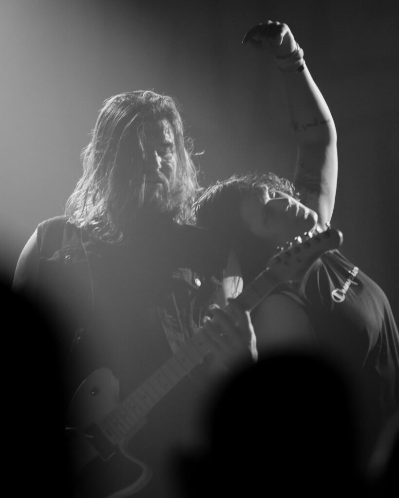 Black-and-white photograph of a long-haired guitarist raising one arm